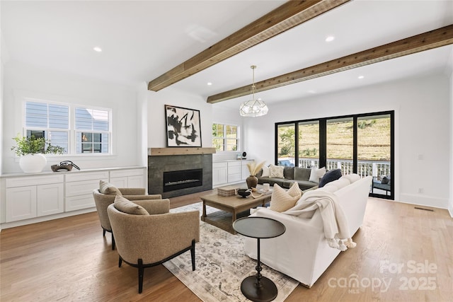 living room featuring a tile fireplace, beamed ceiling, and light hardwood / wood-style flooring