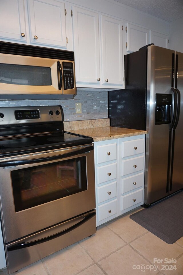 kitchen featuring decorative backsplash, white cabinetry, light stone countertops, light tile patterned floors, and stainless steel appliances