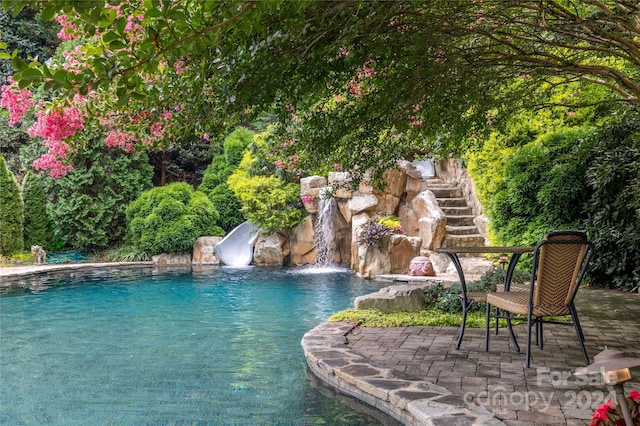 view of swimming pool featuring a patio, a water slide, and pool water feature