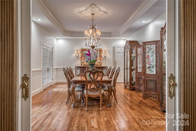 dining area with an inviting chandelier, wood-type flooring, a raised ceiling, and crown molding