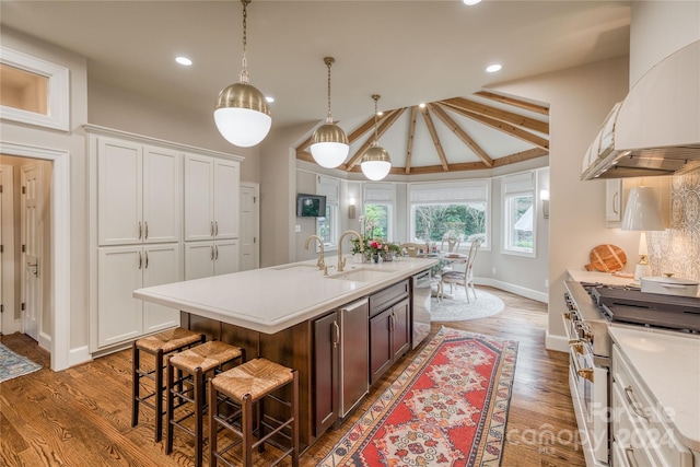 kitchen featuring stainless steel appliances, hardwood / wood-style flooring, vaulted ceiling with beams, a kitchen island with sink, and sink