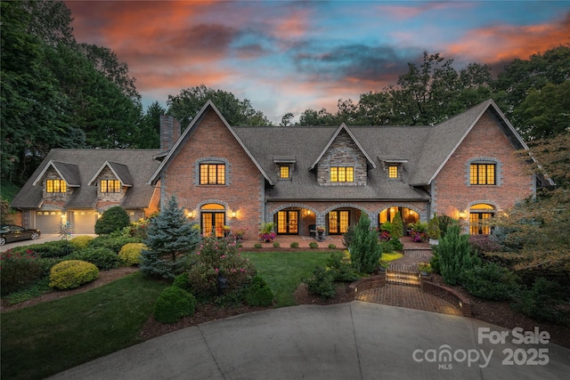 view of front of property with french doors, brick siding, a yard, a chimney, and a garage