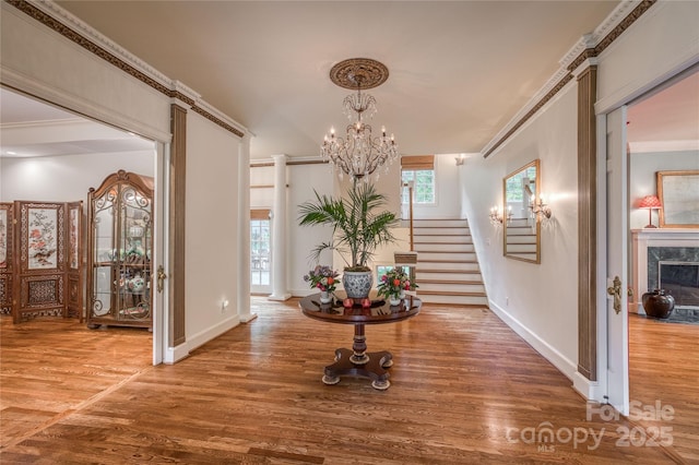 hall featuring baseboards, stairway, wood finished floors, an inviting chandelier, and crown molding