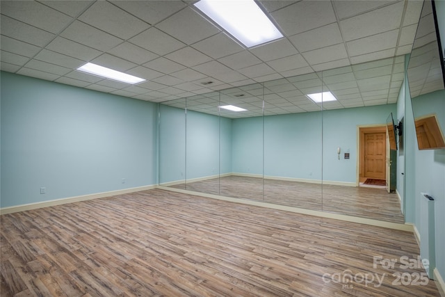 empty room featuring baseboards, a drop ceiling, and wood finished floors