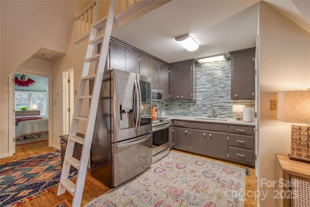 kitchen with light wood finished floors, decorative backsplash, gray cabinets, stainless steel appliances, and a sink