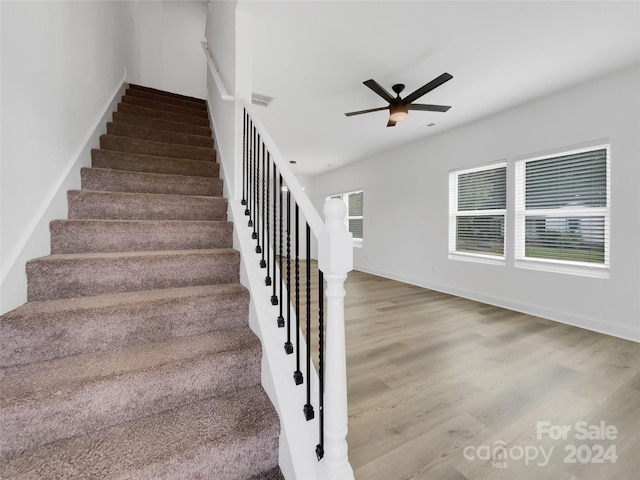 stairs featuring ceiling fan and hardwood / wood-style flooring