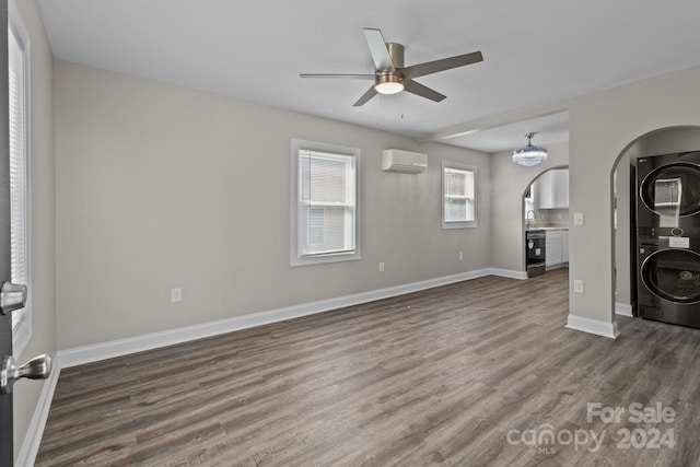 unfurnished living room featuring a wall mounted air conditioner, dark wood-style flooring, stacked washer and clothes dryer, a ceiling fan, and arched walkways