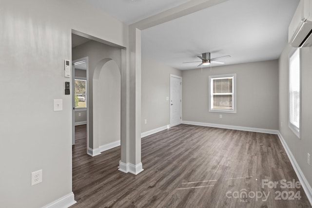 empty room featuring a ceiling fan, a wall mounted AC, arched walkways, and dark wood-style floors