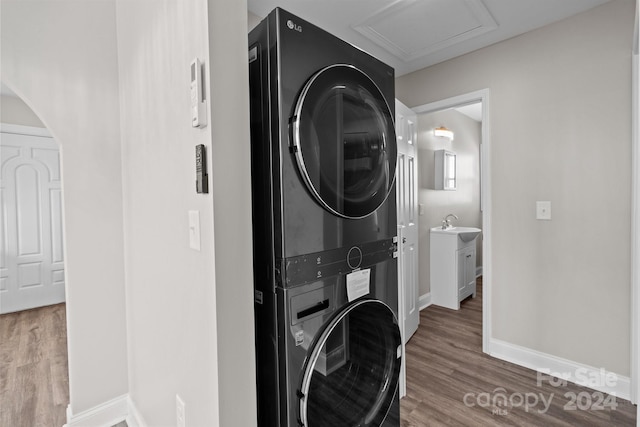 clothes washing area with stacked washer / dryer, baseboards, laundry area, and wood finished floors