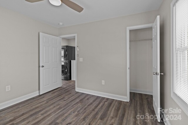 unfurnished bedroom with a closet, ceiling fan, dark hardwood / wood-style floors, and stacked washer and clothes dryer