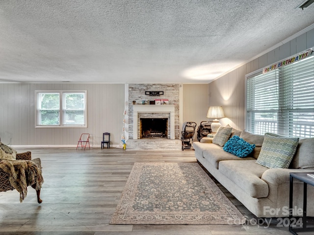 living room with a fireplace, wood walls, a textured ceiling, wood-type flooring, and ornamental molding