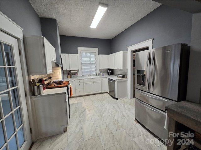 kitchen with a textured ceiling, tasteful backsplash, sink, white cabinetry, and stainless steel appliances