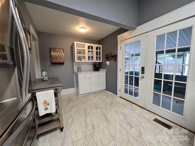 kitchen with stainless steel refrigerator with ice dispenser, backsplash, white cabinetry, and french doors