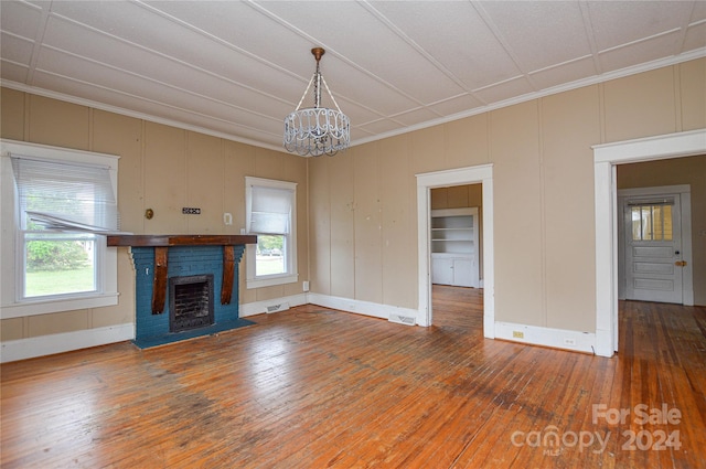 unfurnished living room featuring built in shelves, a brick fireplace, hardwood / wood-style flooring, a notable chandelier, and crown molding