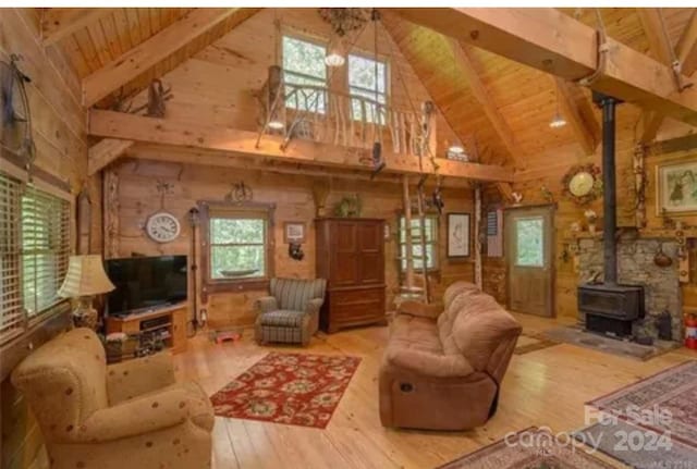 living room with plenty of natural light, beamed ceiling, a wood stove, and hardwood / wood-style flooring