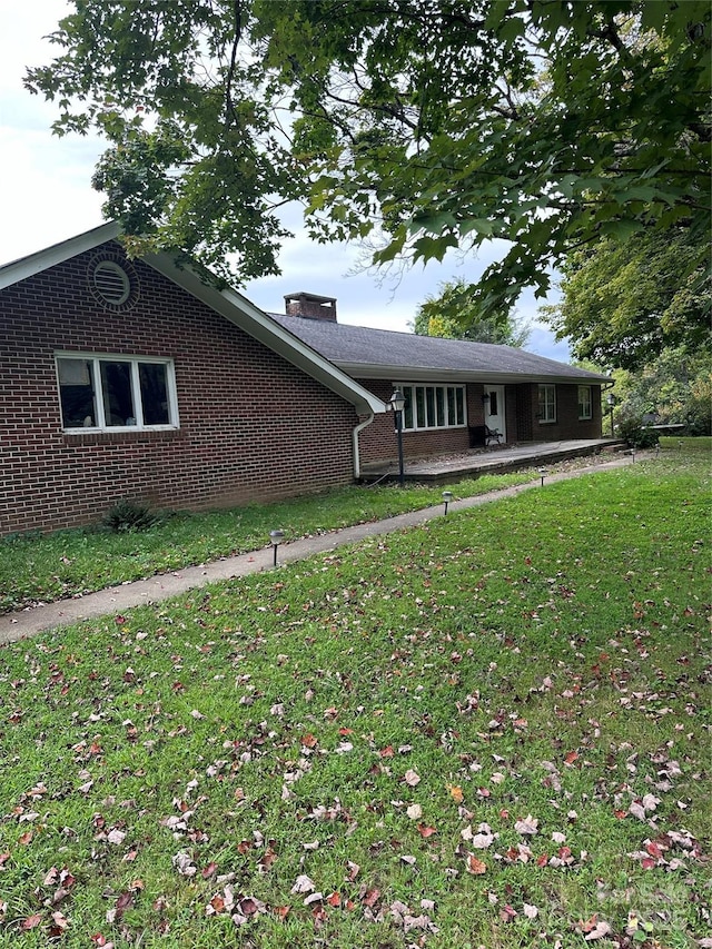 view of front of house featuring brick siding, a chimney, and a front lawn