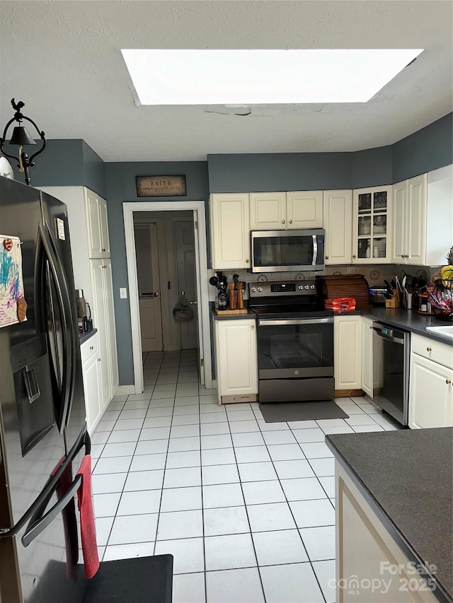 kitchen with stainless steel appliances, dark countertops, glass insert cabinets, white cabinets, and light tile patterned flooring