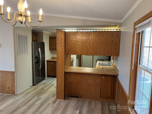 kitchen with brown cabinets, light wood finished floors, stainless steel fridge with ice dispenser, and a textured ceiling