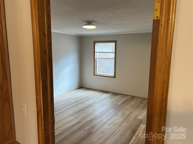 spare room with a textured ceiling, visible vents, crown molding, and wood finished floors