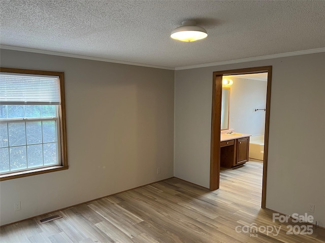 spare room featuring ornamental molding, light wood finished floors, and a textured ceiling