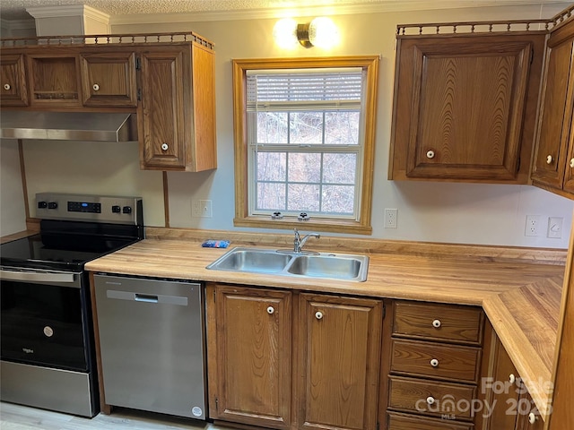 kitchen with stainless steel appliances, light countertops, ornamental molding, a sink, and wall chimney range hood