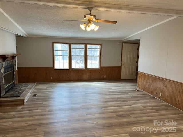 unfurnished living room featuring a wainscoted wall, crown molding, a textured ceiling, wood walls, and a fireplace