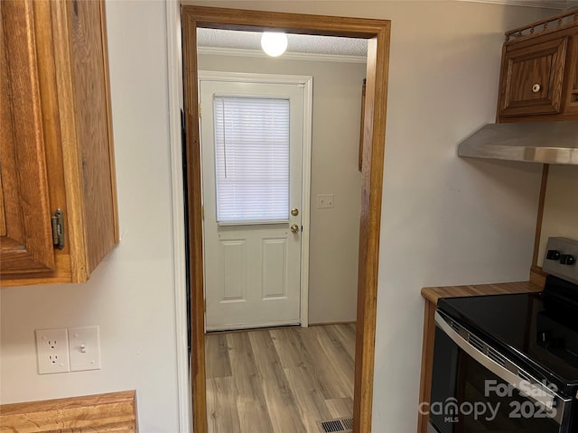 kitchen with brown cabinetry, stainless steel electric range oven, ornamental molding, light countertops, and light wood-type flooring