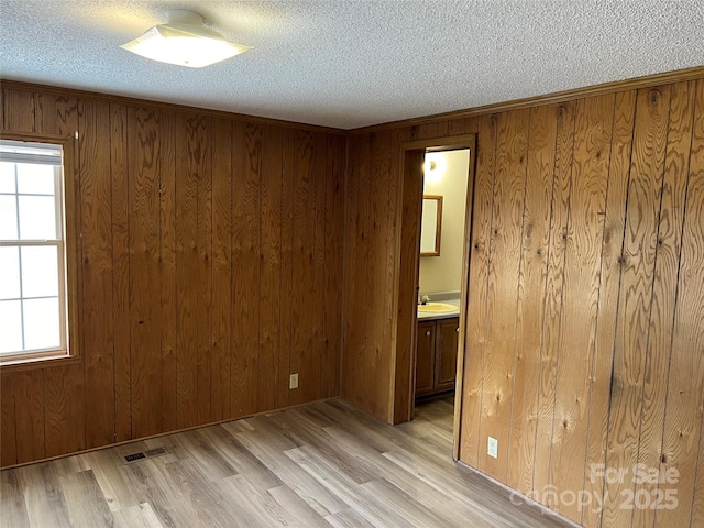 empty room featuring visible vents, a sink, wood walls, a textured ceiling, and light wood-type flooring