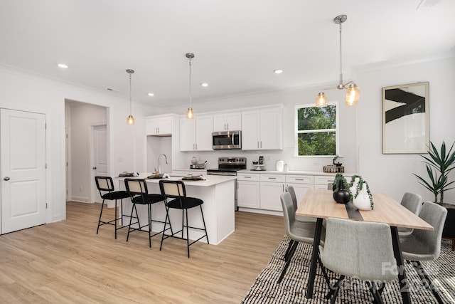 kitchen with a center island with sink, white cabinets, stainless steel appliances, and decorative light fixtures