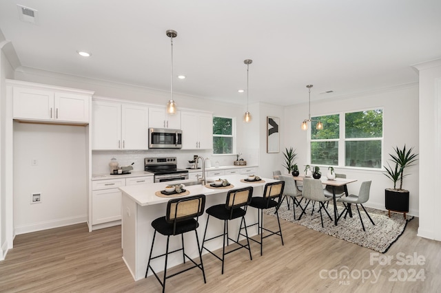 kitchen with pendant lighting, light wood-type flooring, white cabinetry, a center island with sink, and appliances with stainless steel finishes