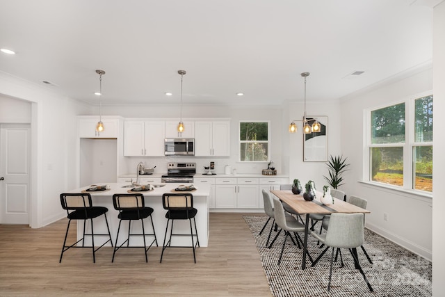 kitchen with hanging light fixtures, a kitchen island with sink, light hardwood / wood-style flooring, and stainless steel appliances