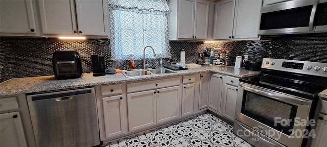 kitchen featuring appliances with stainless steel finishes, light stone countertops, sink, and backsplash