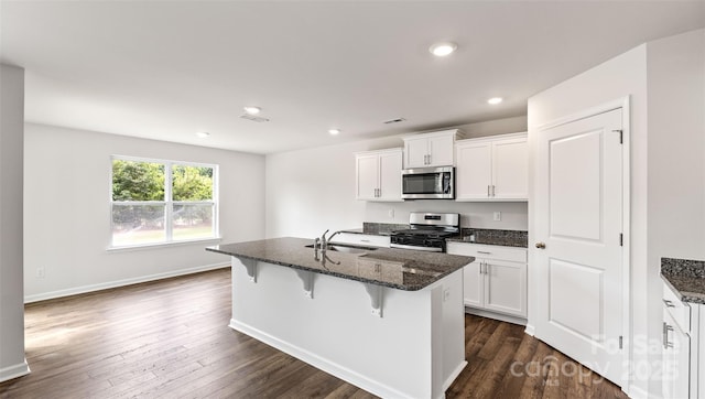 kitchen featuring dark wood-style flooring, dark stone counters, stainless steel appliances, and a sink