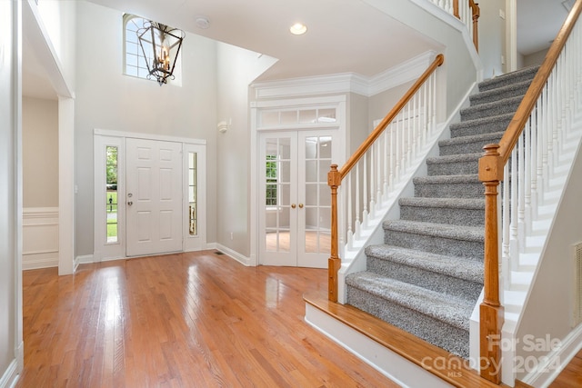 entryway featuring light hardwood / wood-style flooring, an inviting chandelier, crown molding, a high ceiling, and french doors