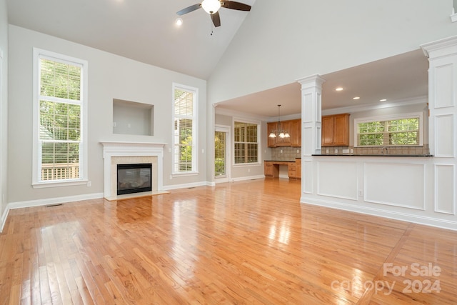 unfurnished living room with a high end fireplace, light hardwood / wood-style floors, ceiling fan with notable chandelier, high vaulted ceiling, and crown molding