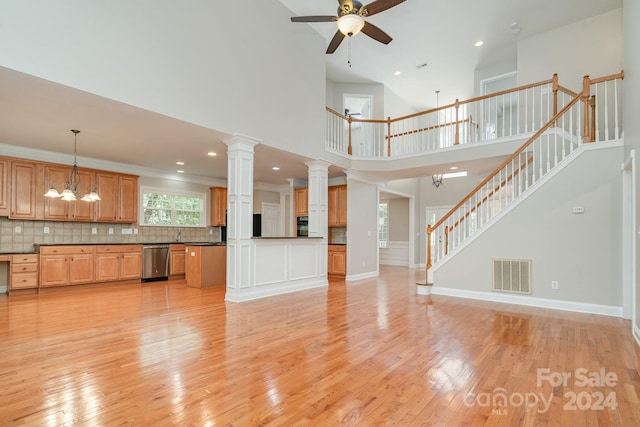 unfurnished living room with decorative columns, ceiling fan with notable chandelier, a high ceiling, and light hardwood / wood-style flooring