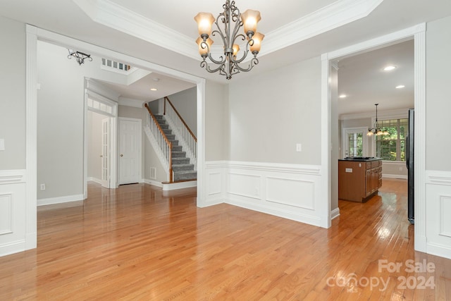 empty room featuring ornamental molding, light wood-type flooring, and a chandelier