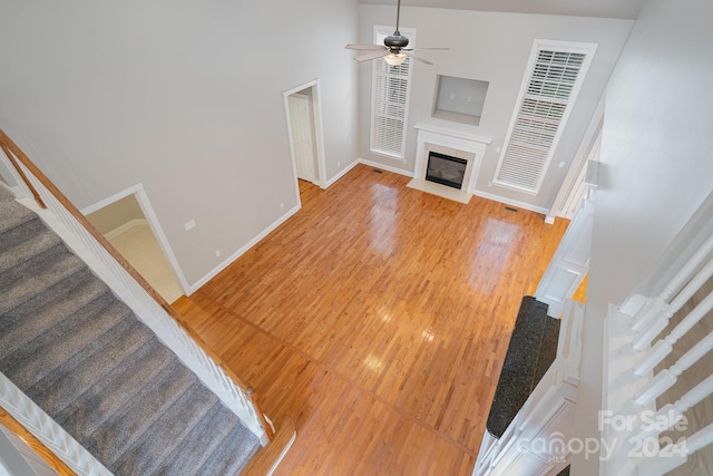 unfurnished living room with a high ceiling, a high end fireplace, ceiling fan, and hardwood / wood-style flooring