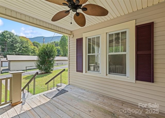 wooden terrace featuring ceiling fan, a lawn, and a mountain view