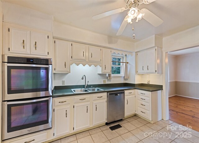 kitchen featuring light tile patterned floors, dark countertops, appliances with stainless steel finishes, white cabinetry, and a sink