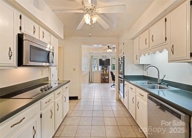 kitchen with light tile patterned floors, stainless steel appliances, dark countertops, white cabinets, and a sink