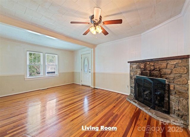 unfurnished living room with crown molding, a wainscoted wall, a fireplace, and wood finished floors