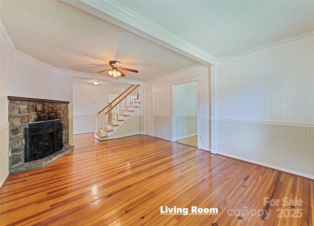 unfurnished living room featuring stairway, wood-type flooring, ornamental molding, and a stone fireplace