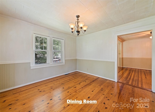 empty room with crown molding, wainscoting, wood-type flooring, and a notable chandelier