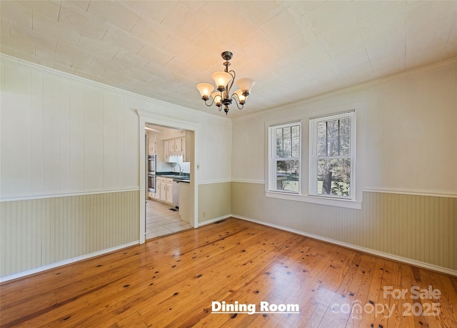 unfurnished dining area with ornamental molding, a sink, a notable chandelier, and light wood finished floors