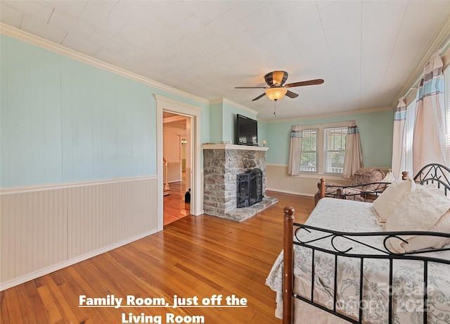 bedroom featuring ornamental molding, wood finished floors, and a stone fireplace