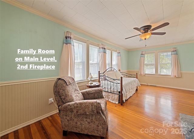 bedroom with ornamental molding, hardwood / wood-style floors, wainscoting, and a ceiling fan