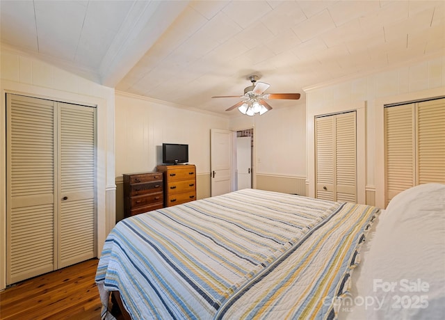 bedroom featuring crown molding, a ceiling fan, two closets, and wood finished floors