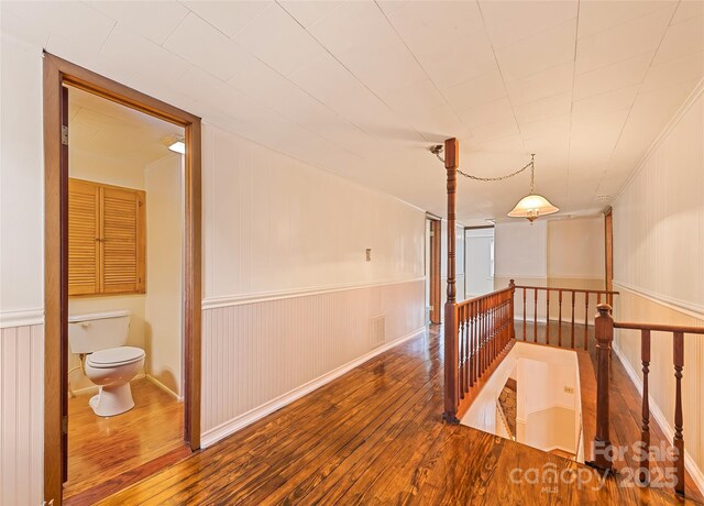 hall featuring wood-type flooring, visible vents, wainscoting, and an upstairs landing