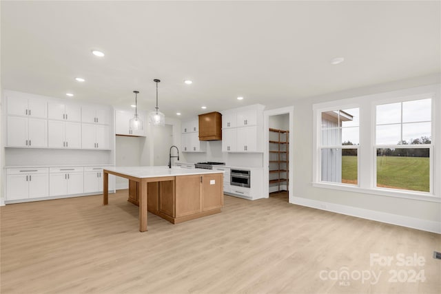 kitchen with a kitchen island with sink, sink, light hardwood / wood-style flooring, white cabinets, and hanging light fixtures